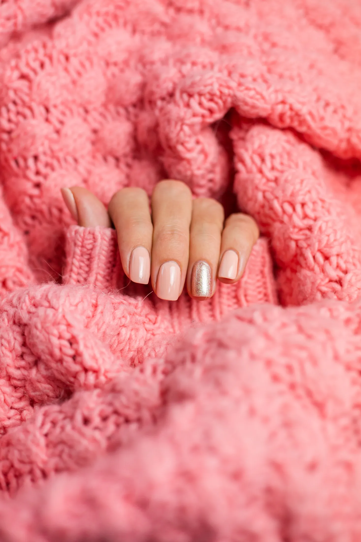 Mains avec une manucure nude et un ongle doré posées sur un pull rose